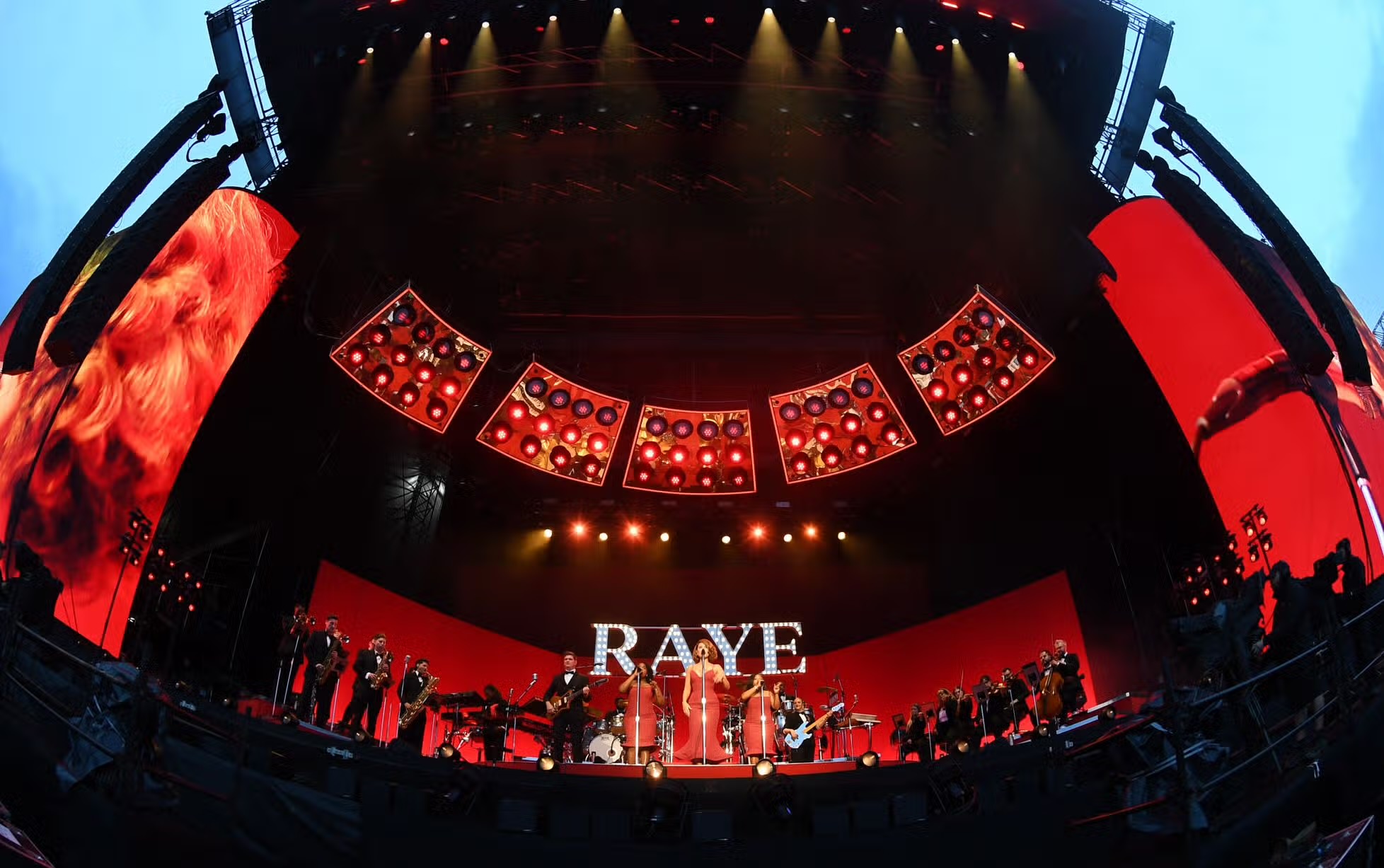 Wide fisheye view of the RAYE stage set with orchestra and red lighting