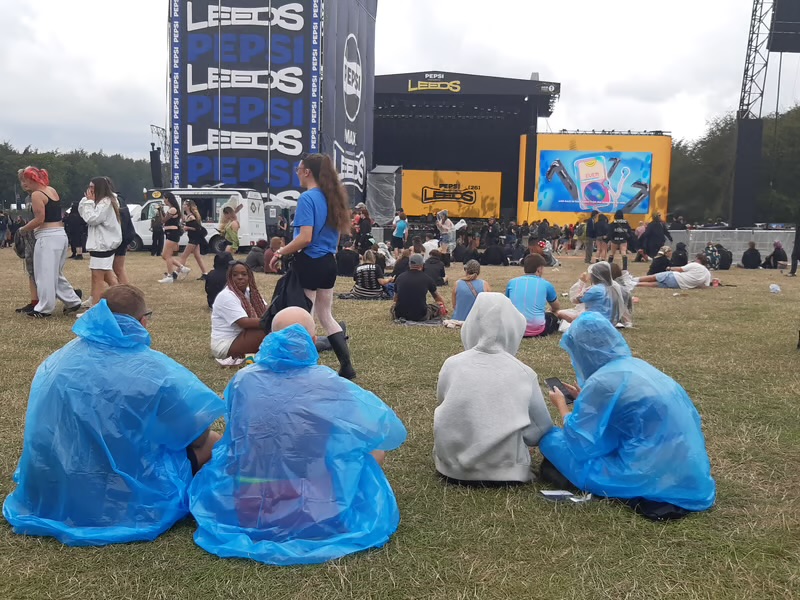Festival-goers in ponchos sitting on the grass in front of the Leeds stage